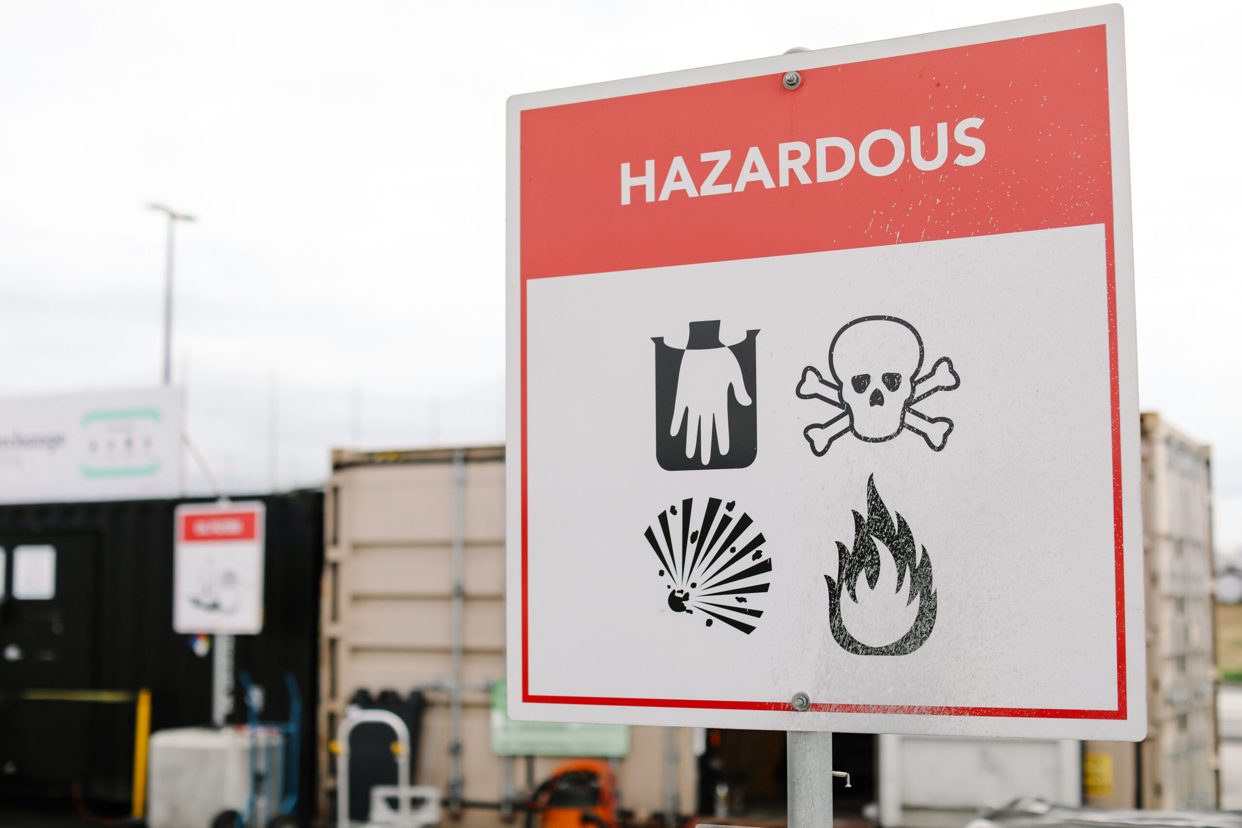Household hazardous waste warning sign at a collection site, showing corrosive, toxic, explosive and flammable hazard symbols.