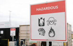 Household hazardous waste warning sign at a collection site, showing corrosive, toxic, explosive and flammable hazard symbols.