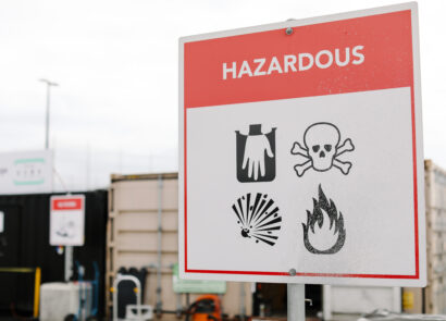 Household hazardous waste warning sign at a collection site, showing corrosive, toxic, explosive and flammable hazard symbols.