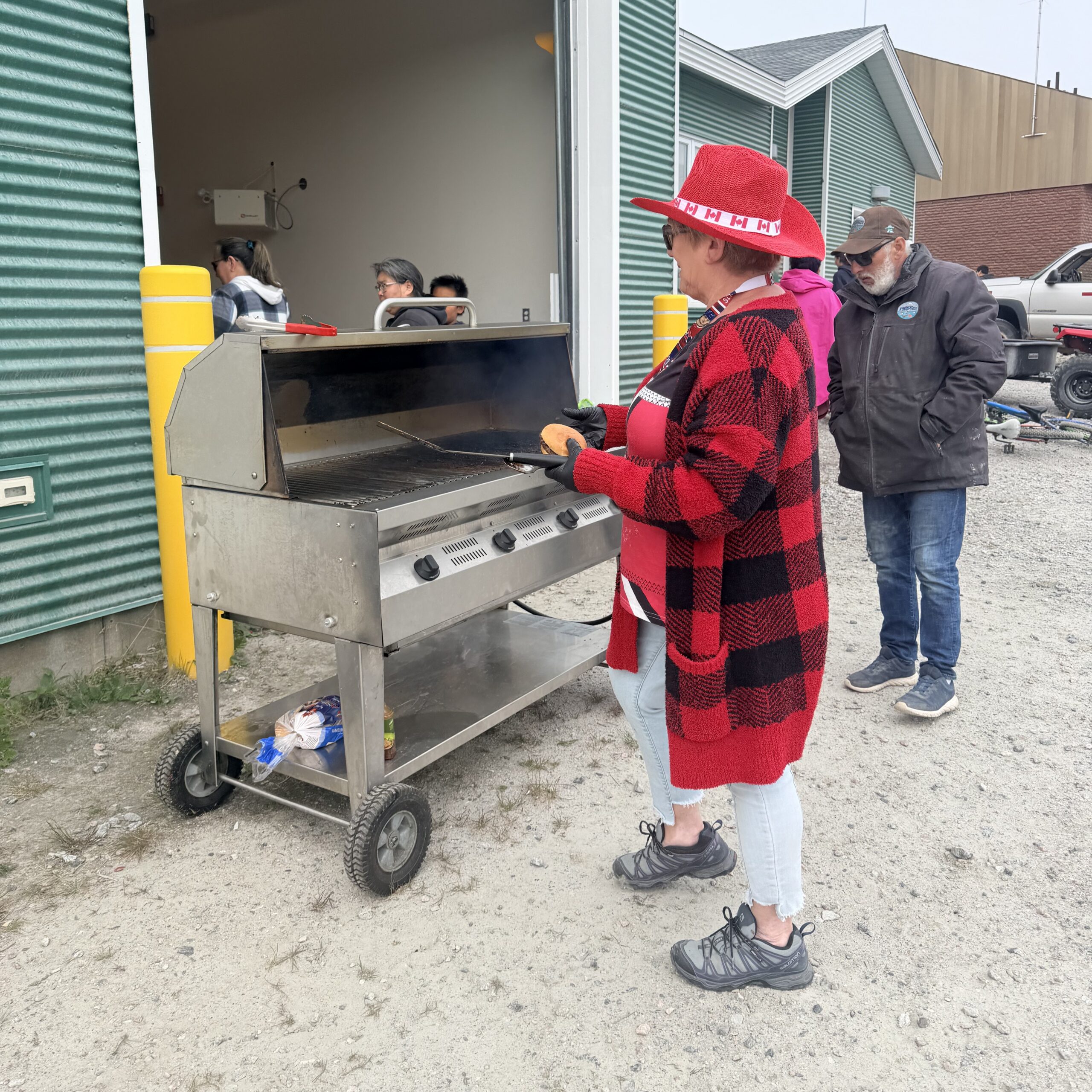 Two volunteers grill hot dogs outdoors during the community celebration