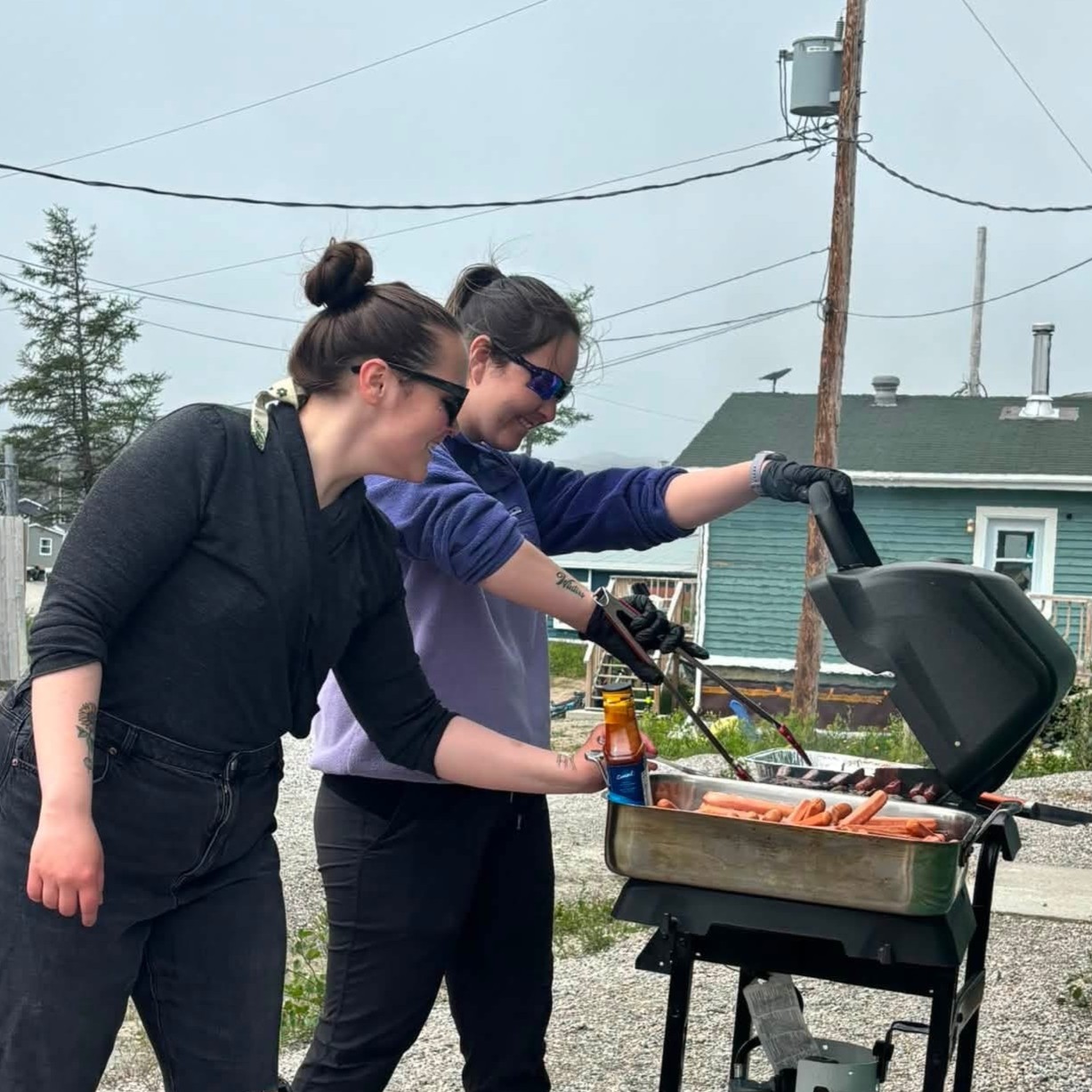 Two Hopedale community members stand beside an outdoor barbecue during the Canada Day recycling event